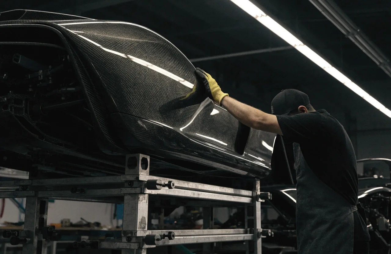 Unbadged hypercar body in profile under a single overhead studio strip light