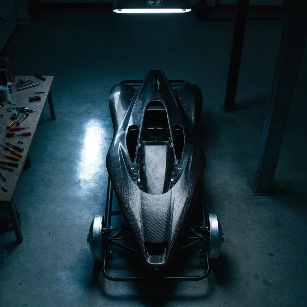Overhead view of a bare carbon monocoque on a build trolley in a night atelier bay