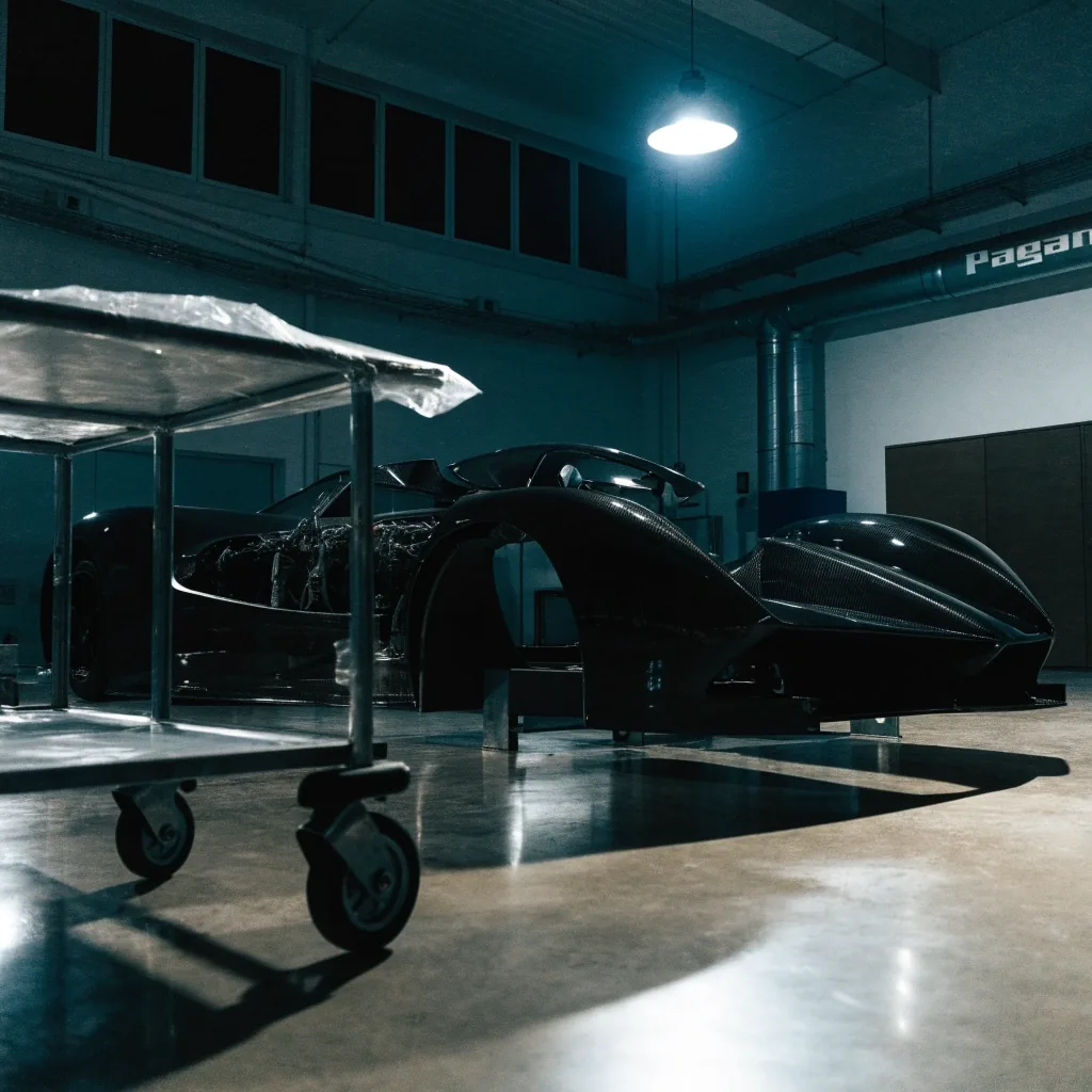 Night interior of an atelier bay with an unbadged car under a single cold overhead lamp